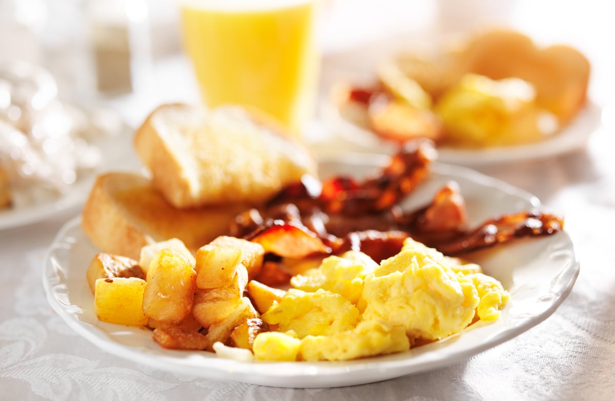 Plate with scrambled eggs, potatoes, toast, and bacon.
